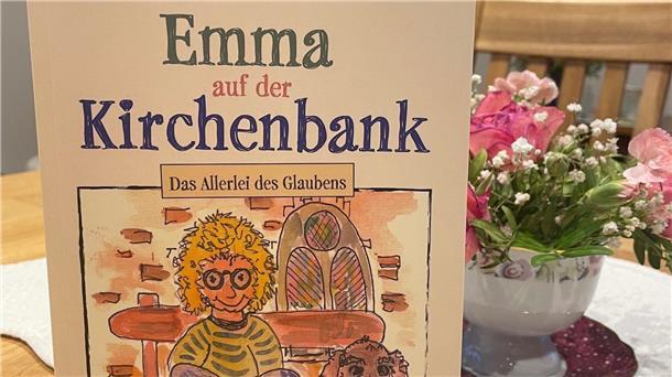 Das Foto zeigt im Vordergrund ein Buch. Dahinter ist eine kleine Vase mit Blumen zu sehen, die auf einem Tisch steht.