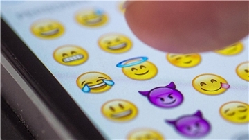 Ein Finger tippt einen Emoji auf dem Smartphone ein.