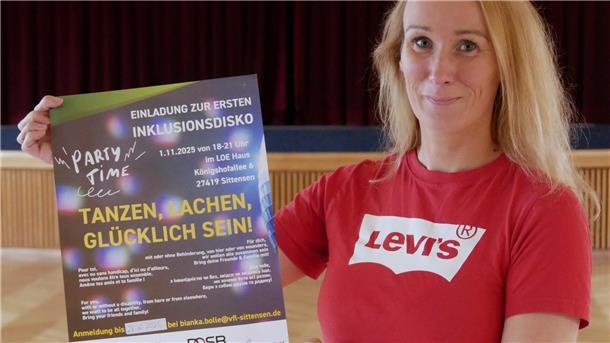 Eine blonde Frau in einem roten T-Shirt hält ein Plakat in der Hand.