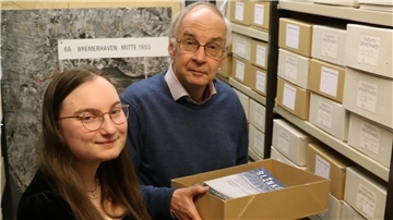 Stadtarchivar Uwe Jürgensen steht mit seiner Nachfolgerin Lea Schnelle neben Akten im Stadtarchiv der Stadt Bremerhaven. 
