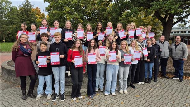 Erwachsene v. l.: Mandy Schaper (Gymnasium Brake), Brigitte Rademacher (IGS Brake), Martina Peters (Polizeistation Elsfleth), Sebastian Jacobs (VBW) und André Gieschen (AllerBus) übergaben den frisch ausgebildeten Busbegleiter:innen ihre Ausweise.