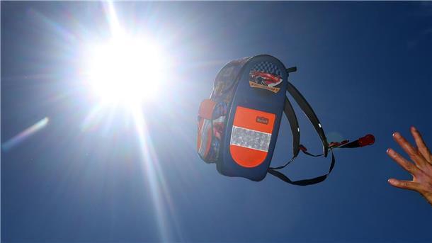 Bremerhaven und das Cuxland: Gibt es vor den Ferien noch Hitzefrei? Eine Hand wirft einen Schulranzen Richtung Sonne.