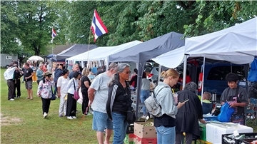 Besucher schlendern über das Thai-Kultur Streetfood Festival in Debstedt. Mehrere Verkaufsstände mit thailändischer Flagge bieten Speisen und Waren an, während Menschen in sommerlicher Kleidung die Stände begutachten.