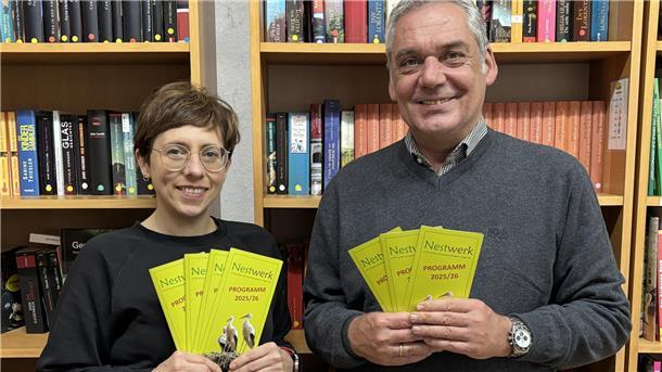 Neues Programm beim Verein Nestwerk: Fokus auf Selbsthilfegruppen Eine Frau und ein Mann stehen vor einem Bücherregal und halten Flyer in den Händen.