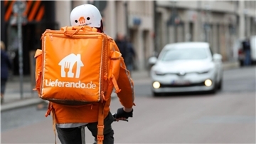 Ein Lieferando-Fahrer fährt auf einem Fahrrad eine Straße entlang. 