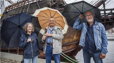 Drei Menschen im Regen mit Regenschirmen. 