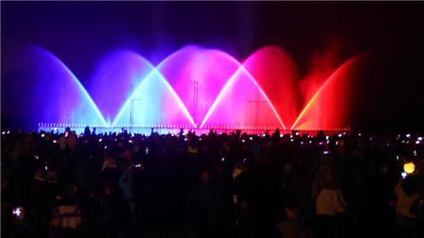 Menschen bestaunen ein farbiges Wasser-Licht-Spektakel. 