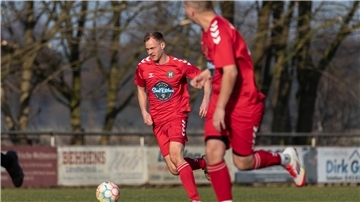 Zwei Männer in roten Trikots laufen hinter einem Ball her.