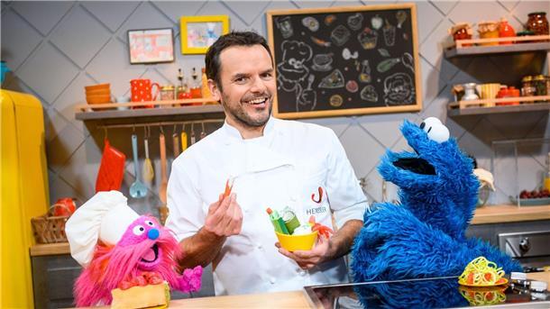 Fernsehkoch Steffen Henssler zwischen den Puppen „Gonger“ (l) und „Krümelmonster“ am Film-Set.