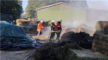 Feuerwehrleute löschen brennende Strohballen.