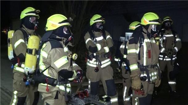 Feuerwehrleute mit Atemschutzmasken stehen vor dem Mehrfamilienhaus in Ronnenberg.