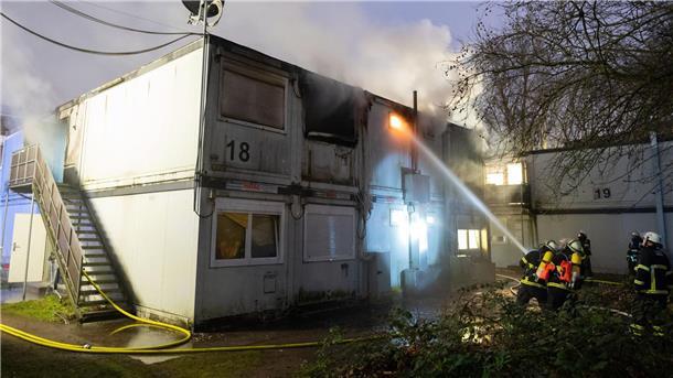 Ein Toter bei Feuer in Hamburger Flüchtlingsunterkunft Feuerwehrleute stehen bei Löscharbeiten vor den verqualmten und teils brennenden Container-Einheiten einer Flüchtlingsunterkunft in Hamburg-Winterhude.
