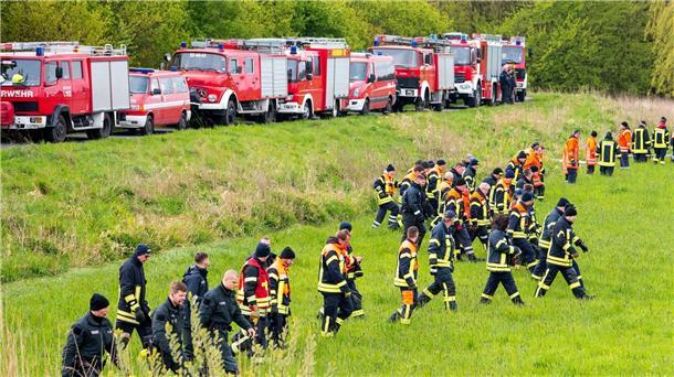 Suche nach Arian jetzt mit Lichtkegeln und Kinderliedern Feuerwehrleute und Polizisten suchen auf einem Feld nach der vermissten Arian.
