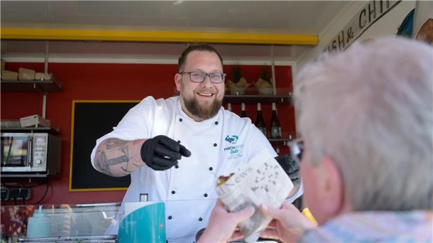 Fischburger, frisch zubereitet und mit guter Laune auf die Hand: Florian Neumann, Sous Chef des Seefischkochstudios, an ungewöhnlicher Wirkungsstätte - im eigens eingerichteten Foodtruck des Kochstudios. Foto: Masorat-f