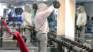 Ein Mann im Hoodie trainiert mit Hanteln.