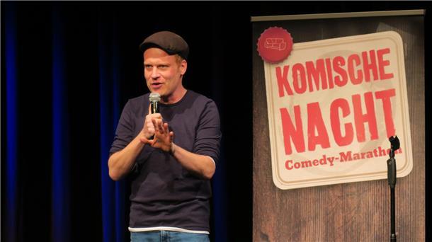 Junger Mann mit Käppi, T-Shirt und Jeans mit Mikro auf der Bühne