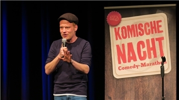 Junger Mann mit Käppi, T-Shirt und Jeans mit Mikro auf der Bühne