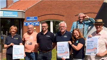 Mehrere Menschen stehen in einer Reihe. Einige von ihnen halten das Poster für die kommende Kutterregatta 2024 in der Hand. 