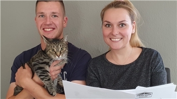 Zwei Personen und eine Katze sehen auf Baupläne.