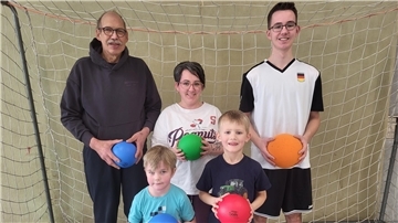 Zwei Erwachsene, ein Jugendlicher und zwei Kinder stehen in einem Fußballtor. In ihren Händen halten sie Bälle. 
