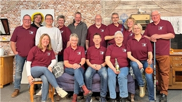 Frauen und Männer in dunkelroten Poloshirts sitzen und stehen auf einer Bühne und lächeln. 
