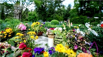 Eine Grableuchte und Blumen liegen auf einem Mühlstein in einem Gräberfeld auf dem Waldfriedhof