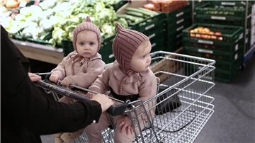 Zwei gleich gekleidete Babys sitzen in einem Einkaufswagen.