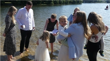 Eine Familie steht im Wasser im Uferbereich des Sieverner Sees, während ein junges Mädchen gerade mit Seewasser getauft wird.