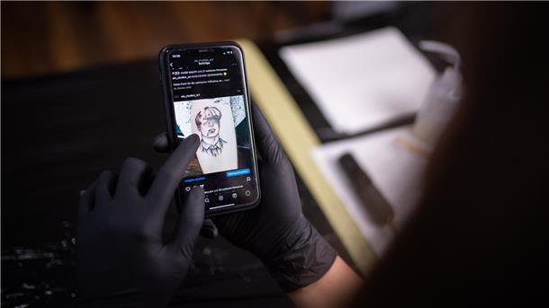 Diese junge Frau findet im Tattoo-Studio auf dem Dorf ihre Bestimmung Auf dem Display eines Handys ist ein Tattoo Motiv zu sehen.