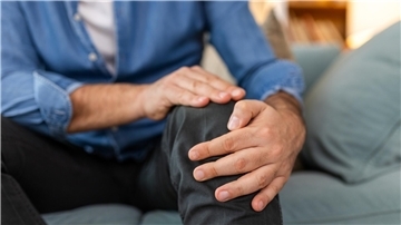 Älterer Herr hält sein linkes Knie fest.