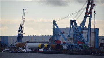 Fundamente für Offshore-Windräder werden vor dem Werk von Steelwind Nordenham auf einen von Schleppern gezogenen Ponton verladen.