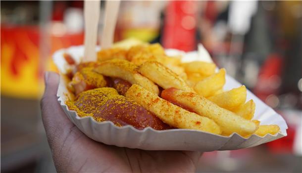 Eine Hand hält eine Papp-Schale mit Pommes und Currywurst.