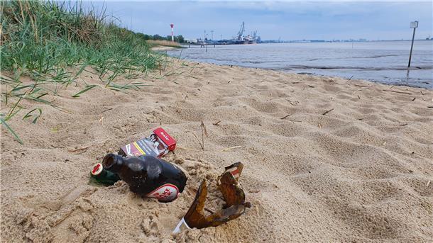 Glasflaschen und eine Zigarettenschachtel liegen am Nordenhamer Weserstrand im Sand.