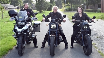 Drei Frauen auf Motorrädern stehen nebeneinander auf einer Straße.