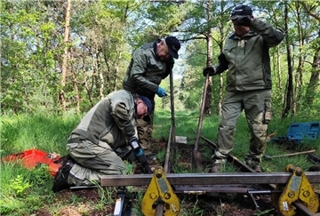 Drei Männer in Arbeitskleidung führen Reparaturarbeiten an einem Gleis der Moorbahn im Wald durch. Werkzeuge und Geräte liegen am Rand der Strecke.