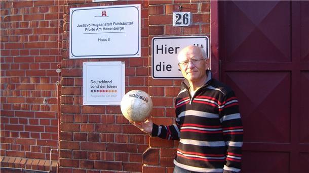 Gerhard Mewes aus Klein Meckelsen steht mit einem Fußball in der Hand vor einer Pforte der Haftanstalt Hamburg-Fuhlsbüttel, im Volksmund „Santa Fu“ genannt. Über seine Zeit als Fußballtrainer im Knast hat der 77-Jährige bereits zwei Bücher verfasst.