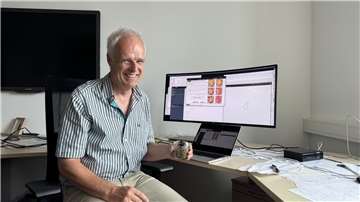 Ein Mann sitzt mit einem Glas Sand in der Hand vor einem Monitor.