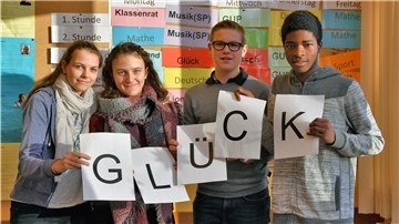 Drei Schüler halten Zettel in der Hand, auf den das Wort Glück buchstabiert ist.