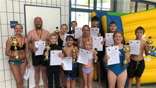 Gruppe von Menschen mit Pokalen und Urkunden im Schwimmbad.