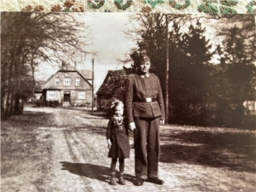 Ein Mann in Uniform und ein Mädchen stehen auf einer Straße und blicken in die Kamera.