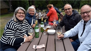 An einem Tisch im Freien sitzen zwei Männer und zwei Frauen bei einem Glas Wein.