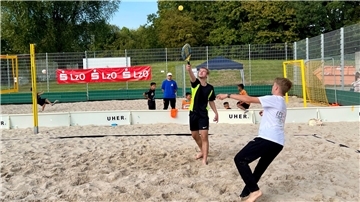 Zwei Männer spielen auf einem Beachfeld ein Spiel mit Schlägern und Ball. 