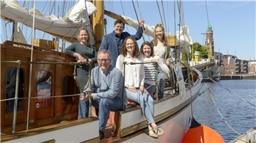 Mehrere Menschen stehen lächelnd auf einem Boot im Becken des Neuen Hafens. 
