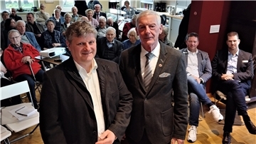 Zwei Männer vor einer Gruppe von Menschen. Hans-Rudolf Mengers (rechts) gratuliert seinem Nachfolger Karsten Hinrichs zur einstimmigen Wahl zum neuen Vorsitzenden des Rüstringer Heimatbunds.