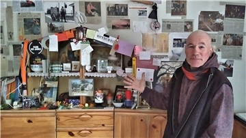 Harry Wallis vor einer Pinwand mit Zeitungsausschnitten und kleinen Gegenständen, die ihm von seinen "Fans" geschenkt wurden.
