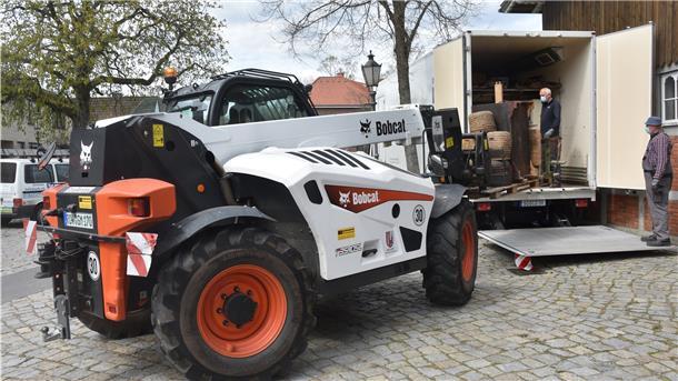 Das Foto zeigt, wie Museumsexponate mit Hilfe freiwilliger Helfer und eines Bobcats in die mobile Klimakammer gebracht werden. 