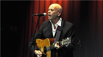 Mann mit Gitarre steht an einem Mikrofon und singt.