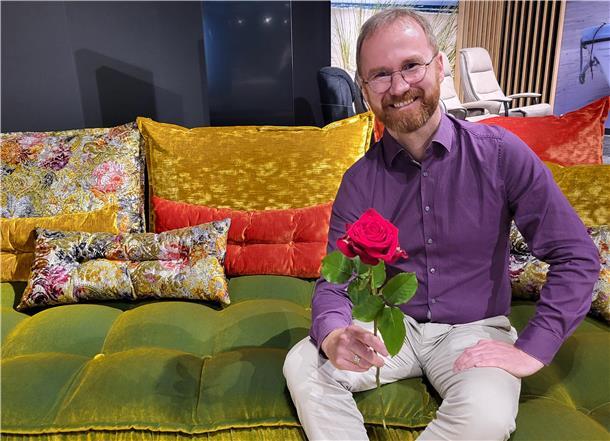 Ein Mann sitzt mit einer roten Rose auf einem bunten Sofa, Hendrik Lenz vom Wohncenter in Nordenham
