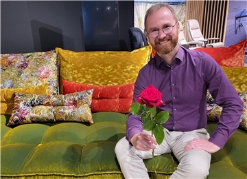 Ein Mann sitzt mit einer roten Rose auf einem bunten Sofa, Hendrik Lenz vom Wohncenter in Nordenham
