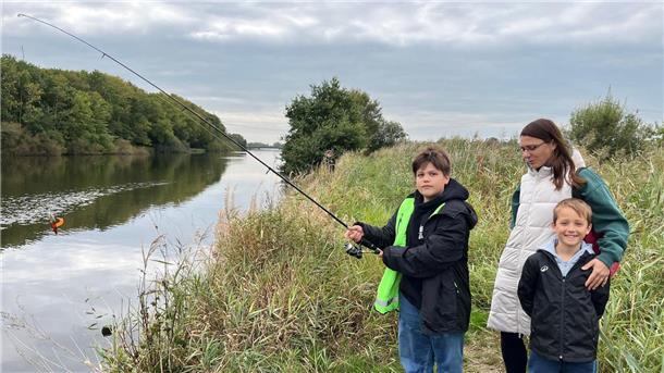 Forellenjagd an der Lune: Was Nachwuchsangler aus dem Wasser holen Ein Junge beim Angeln. Bei ihm eine Frau, seine Mutter und sein jüngerer Bruder.